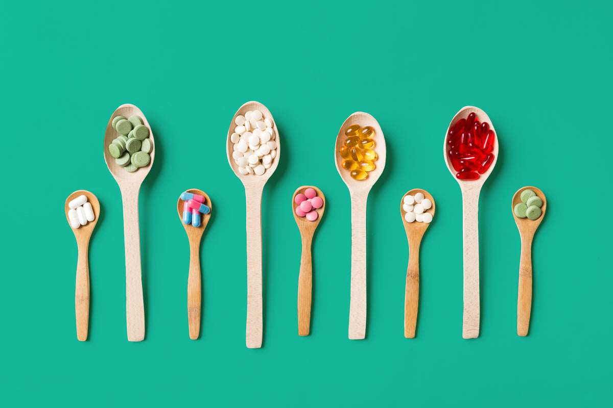 Various vitamin and supplement pills, tablets and capsules arranged on wooden spoons